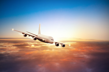 Naklejka na ściany i meble Airplane flying above clouds in dramatic sunset