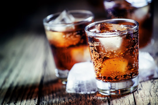 Rum and cola and ice, dark wood background, selective focus, sha