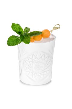 Faceted white cocktail glass decorated with melon on stick and mint leaves