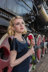 Fototapeta na wymiar Blonde girl is waiting for the locomotive rose retro old train station