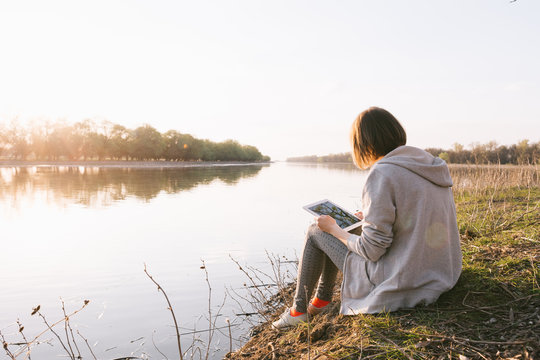 Young girl works with the tablet on the banks of the river