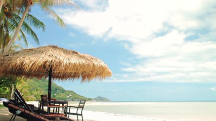 Sunbeds and a table under straw umbrella at the tropical sand beach