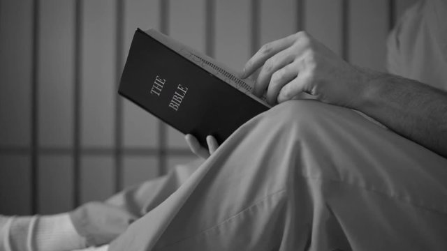 Black and white dolly shot of an inmate reading a bible in prison