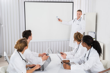Doctor Pointing At Board In Front Of His Colleagues