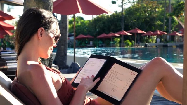 Young woman reading menu sitting on sunbed
