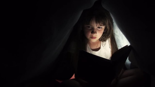 Girl reading book under blanket