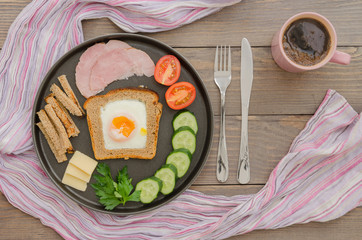breakfast with scrambled eggs, ham, bread, cheese, vegetables and coffee on a wooden background