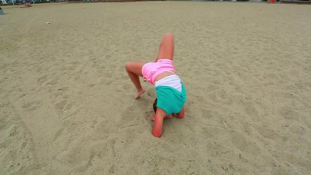 Slow motion of young girl practicing gymnastics on the sand at beach