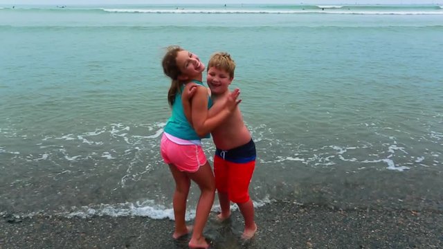 Slow motion of brother and sister playing by ocean at beach