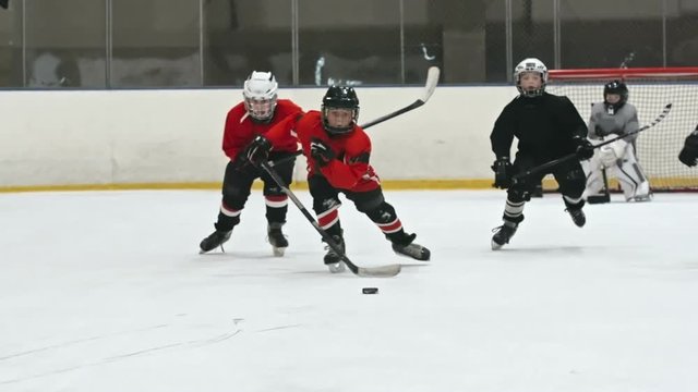 Little boys playing hockey on ice rink. One player in red uniform skating and pushing the puck with stick. Filmed with Sony Nex 700