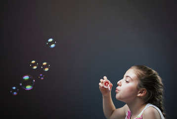 Lovely little girl blowing soap bubbles on dark background