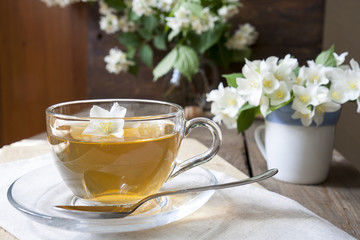 Transparent glass cup of tea with jasmine and blooming jasmine branch in blue ceramic cupon wooden board