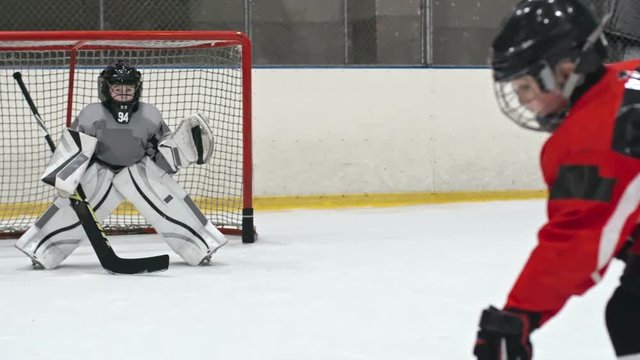 Little hockey goaltender in protective uniform falling down on ice rink while trying to catch the puck in slow motion