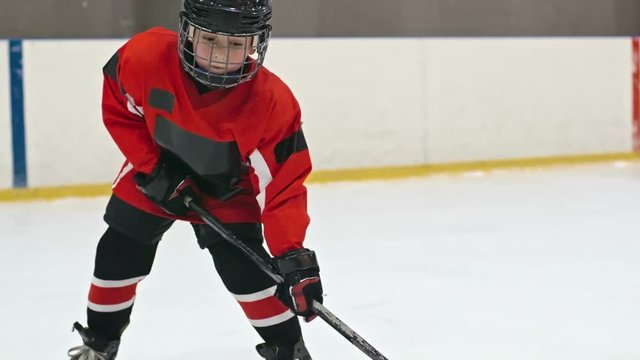 Little hockey player standing on ice rink and shooting the puck into the net