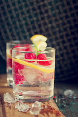 Homemade summer cold raspberry lemon cocktail with sparkling water and crushed iced in glasses on a vintage background, closeup, toned