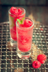 Homemade summer cold raspberry cocktail with ice, berry syrup and alcohol in glasses on a vintage background, closeup, toned