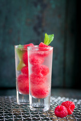 Homemade summer cold raspberry cocktail with ice, berry syrup and alcohol in glasses on a vintage background, closeup