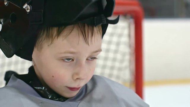 Close up of little boy in hockey uniform putting on his helmet and looking in front of him
