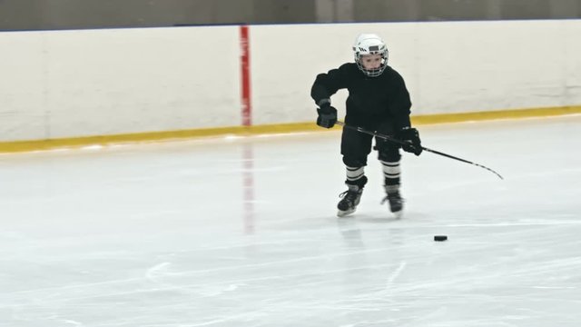 Two boys playing hockey in winter arena; one of them handling the puck and then performing slap shop