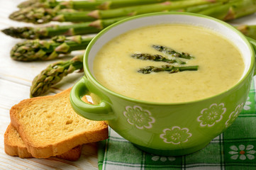 Green asparagus cream soup on wooden background.