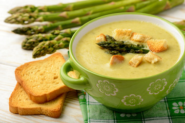 Green asparagus cream soup on wooden background.