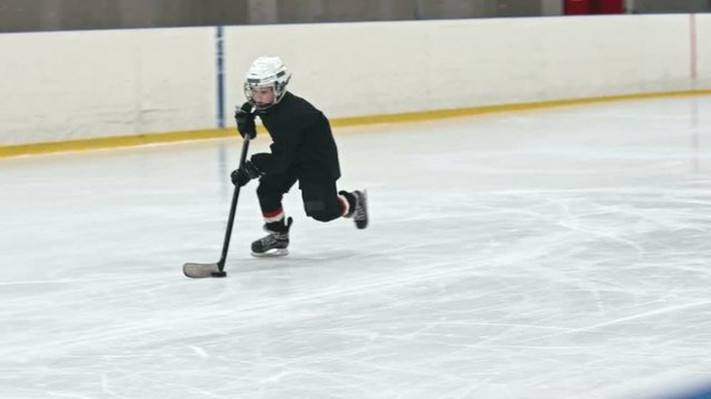 Little hockey player handling the puck and scoring the goal while playing on the ice rink