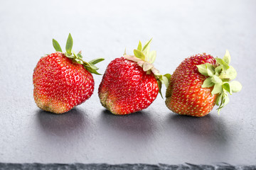 Three ripe red strawberries on slate blackboard