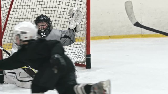 Little hockey goaltender in protective uniform falling down on ice rink while playing the game