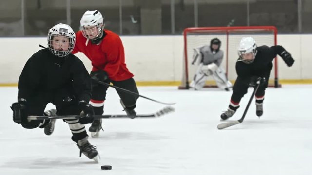 Boy in black uniform skating towards the camera and handling the puck whiles his opponent and teammate trying to reach him. Filmed with Sony Nex 700