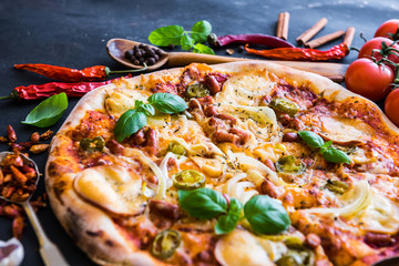 tasty pizza on a black background with spices and vegetables