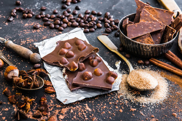 Chocolate with nuts and spices in the spoons on a dark table