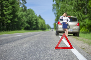 Red triangle sign on the road and Young woman calling for car as