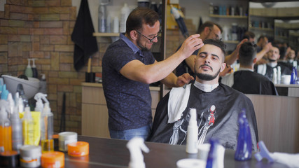Hipster hairstyles in the salon. Professional barber uses a straight razor to make the beard trend...