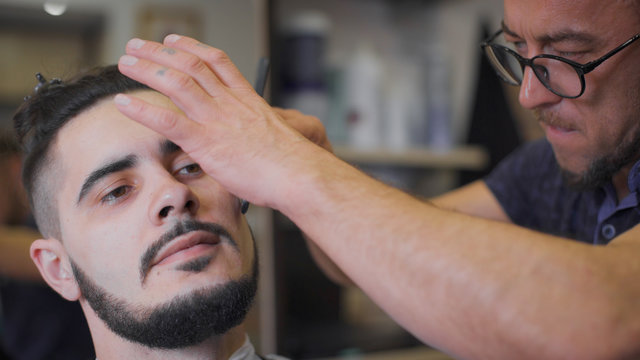 Hipster hairstyles in the salon. Professional barber uses a straight razor to make the beard trend form.