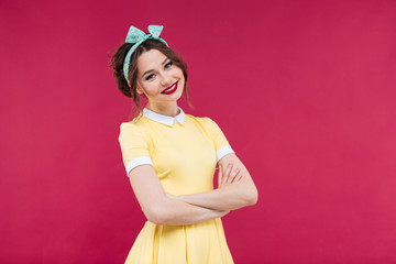 Smiling young woman in yellow dress standing with arms crossed