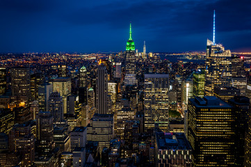 Aerial view of midtown Manhattan at night, the heart of a financial empire that dominates the business world, with every building vividly colored in shades of blue and green in NYC