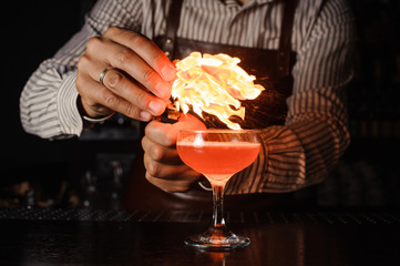 The bartender makes flame above cocktail