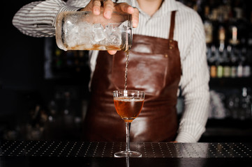 barman pouring alcoholic cocktail in glass