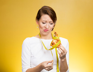 sad woman looking at fatty pizza with measuring tape around craving junk food