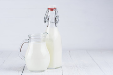 Jar with milk and vintage bottle of milk on white wooden table background