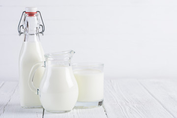 Milk bottle with jug and glass of milk on white wooden table