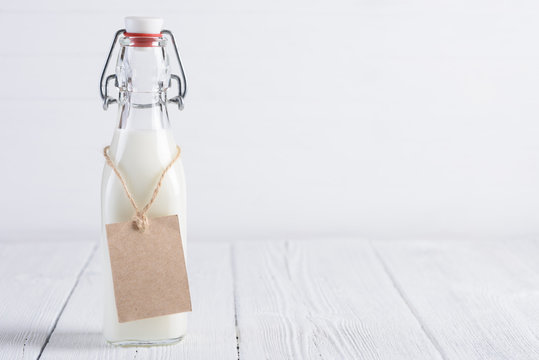 Bottle of milk with blank paper tag on rope on white painted wooden table still life