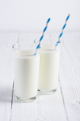 Two glasses of milk with blue stripped paper straw on white wooden table still life