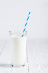 Glass of milk with paper striped straw on white wooden table