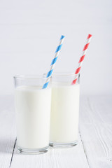 Two glasses of milk with blue and red stripped paper straws on white wooden table still life