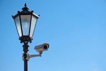 Fototapeta na wymiar CCTV surveillance camera mounted on vintage street lantern over blue sky background