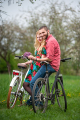 Fototapeta premium Two smiling lovers standing with bicycles and holding hands in the spring garden, against the background of trees and fresh greenery