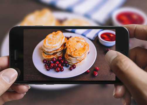 Taking picture of pancakes with mobile phone. Phone in male hands.On the plate there is pancakes with berries and honey.