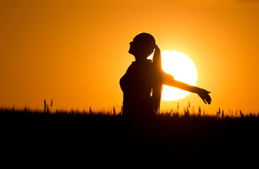 Silhouette of girl with raised hands at sunset