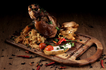 Grilled pork knuckle served with braised cabbage, fresh cherry tometoes and mustard served on wooden board on rustic wooden counter
